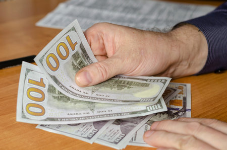 Hands of a male with dollars in close-up. A man counts money while sitting at the table. A sheet of...