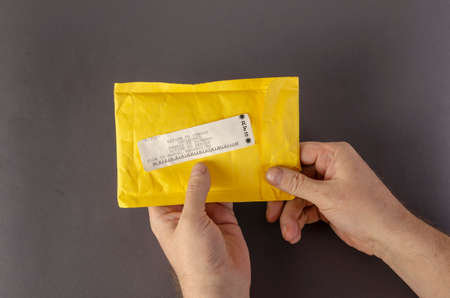 Hands hold a yellow mail bag that says RETURN TO SENDER. Undelivered package on a gray background. Top view, no people.の写真素材