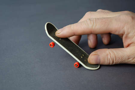 Mini skate and hand on a gray background. Male hand plays finger skateboard. Close-up, selective focus.の写真素材