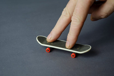 Mini skate and hand on a gray background. Male hand plays finger skateboard. Close-up, selective focus.の写真素材