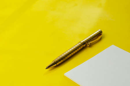 White square blank tear-off note paper and pen on yellow background. A small stack of paper stickers and a gold-colored metal pen on a solid background. No people.の写真素材