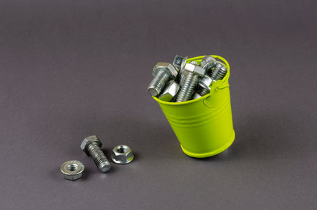 Bolts, nuts and a small green bucket on a gray background. A bucket full of shiny metal hardware. Close-up, selective focus.の写真素材