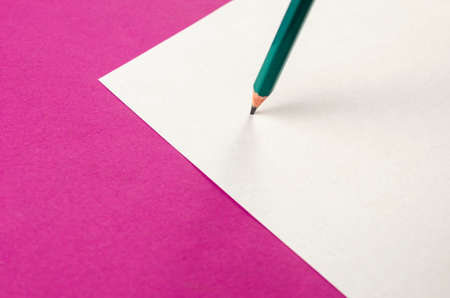Blank paper and pencil on a pink background. A green wooden pencil stands on a white sheet of paper. Top view from an angle, selective focus.の写真素材