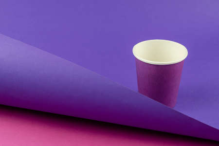Lilac paper cup on a two-color abstract geometric background. Empty glass for drinks on a purple-pink background with a diagonal shadow. Selective focus.の写真素材