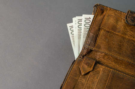 Brown leather wallet with money on a gray background. Euro banknotes are peeking out of the Open Wallet.の写真素材
