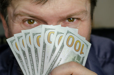 The person hides her face behind money. A middle-aged man with gray hair covers his entire face in...