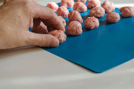 Male hand puts meatballs on a blue surface. A middle-aged man is folding meatballs formed from raw minced meat. Selective focus.の写真素材