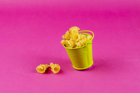 Green metal bucket and dry Gigli or campanelle pasta on pink background. The small bucket of pasta is tilted. Close-up, selective focusの写真素材