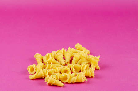 Dry Gigli or campanelle pasta on pink background. A portion of the sprinkled pasta. Close-up, selective focus.の写真素材