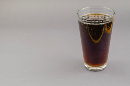 Glass of soda on a gray background. A full glass of refreshing drink. Side view, copy space.