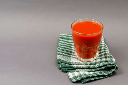A full glass of tomato juice and a green checkered napkin on a gray background. Ready-to-drink beverage. Side view at an angle. Selective focus.の写真素材