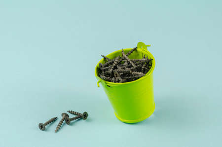 Screws and a small green bucket on a blue background. Black metal hardware in a bucket. Close-up, selective focus.の写真素材