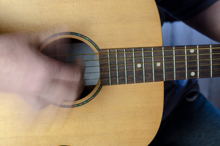 Hand plays the acoustic guitar, motion blur. Close-up of the neck and soundboard of a yellow guitar....
