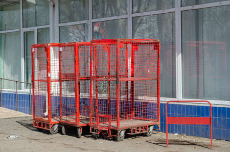 Red cages on wheels outside the building. Storage cages against a glass wall. Logistics and warehouse storage. Sunny day. No people.の写真素材