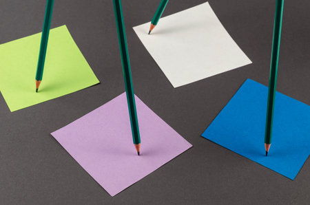 Standing pencils and multicolored note stickers on a gray background. A group of green pencils...