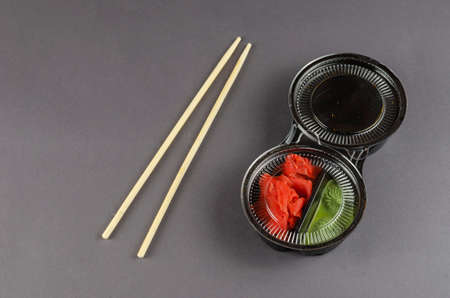 Disposable plastic container with sushi sauces and bamboo sticks on a gray background. Ginger Wasabi And Soy Sauce In Take Away Box. Takeaway food.の写真素材