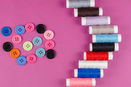 Multicolored thread spools and buttons on purple background. A set of thread. Ten spools. Random buttons. Top view, flatlay.の写真素材