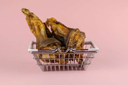 Shopping basket with dog treats on a pink background. Chewy treats in metal basket. Dried beef ears for pets. Pet supplies. Side view from an angle.の写真素材