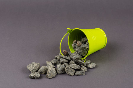 Gravel and a small green bucket on a gray background. Rubble poured out of the fallen bucket. Close-up, selective focus.の写真素材