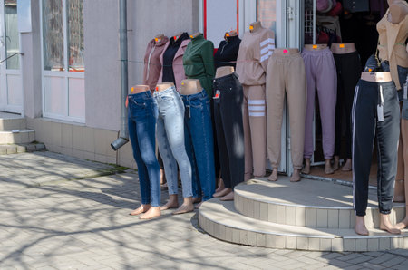 Mannequins and legs of female mannequins in robes outside the store. Jeans, tracksuits, skirts, trousers and other women's clothing with price tags. Daytime.の写真素材