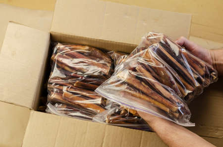 Men's hands pull dried dog treats out of a cardboard box. Packs of dried bovine penis for pets. Small business. An angled view from above.の写真素材