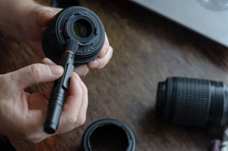 Care of photographic equipment. Cleaning the lens from dust. Men's hands with a special brush remove dirt and dust from the lens.の写真素材