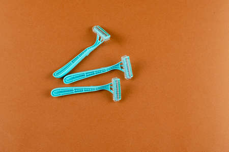 Blue plastic razors on a brown background. Three new razor. Top view, flat lay. Copy spaceの写真素材