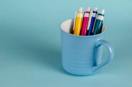 Blue striped mug and a set of pens on a blue background. Empty new ceramic mug and a set of multi-colored plastic pens in it. Minimalism. Close-up.の写真素材