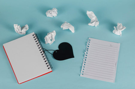 Black heart symbol and open notepad on a blue background. Crumpled pieces of white paper and a torn...