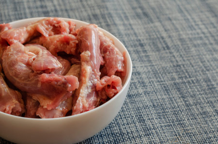 Raw chicken necks in a white ceramic bowl on a blue background. Portion of chicken offal close-up....