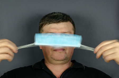 Portrait of an adult male rotating a medical mask in front of his face. A middle-aged man with short...