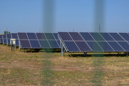 Rows of solar panels behind a fence in a field. Blurred outlines of the fence against the backdrop...