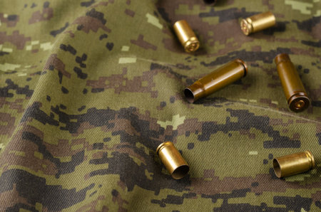 A few random casings on camouflage cloth. A group of pistol and rifle empty casings lie on military...