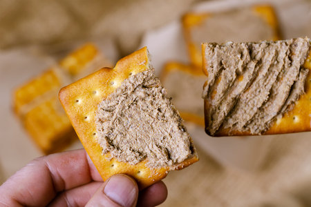 High angle view of a hand holding a cracker with liver pate. Man holding a cracker cut in half with...