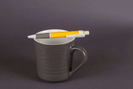 Gray striped mug and yellow pen on a gray background. An empty new ceramic mug with a plastic pen...