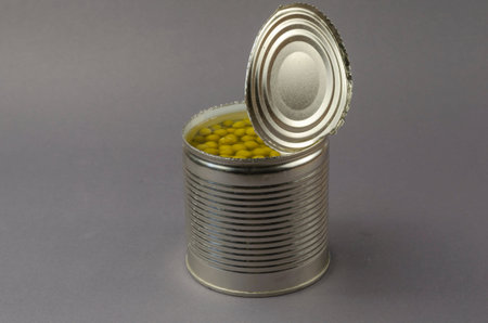 Open tin can on a gray background. Canned green peas. The can was opened with a knife. Ready-to-eat...