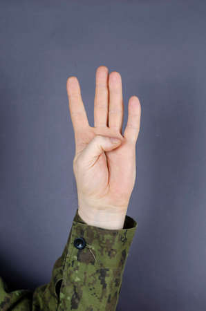 Hand in camouflage shows gesture with his fingers on gray background. Four fingers are raised up. The designation of the number four in the military. Army gesture language.の写真素材