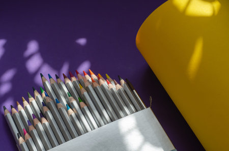 Light and shadow composition with a set of gray wooden pencils on a yellow and blue background. Open-box with multicolored watercolor pencils and paintbrush. View from above at an angle.の写真素材