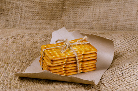 A stack of rectangular crackers tied with string on sackcloth. Close-up of crispy, salty, ready-to-eat crackers. Piece of wrapping paper with torn edges.の写真素材