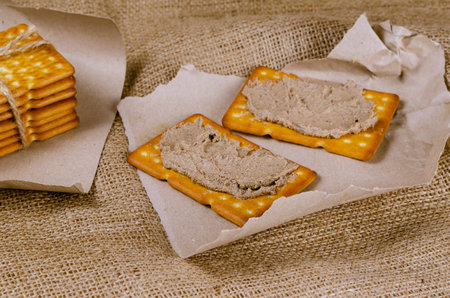 Rectangular liver pate crackers on a burlap sack. Ready-to-eat food on pieces of wrapping paper with...
