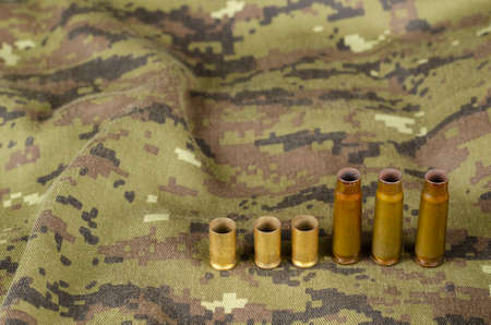 A few random casings on camouflage cloth. A group of pistol and rifle empty casings lie on military uniforms. Army theme.の写真素材