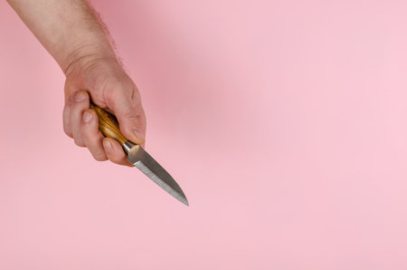 Small Knife and Hand on a pink background. The man is holding a metal kitchen knife with a wooden handle. Side view. Copy space.の写真素材