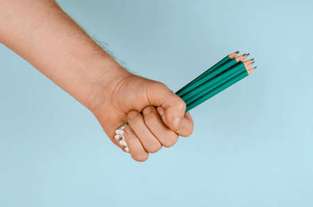 A hand and green wooden pencils on a blue background. Man holding many pencils. Side view. Close-up. Selective focus.の写真素材
