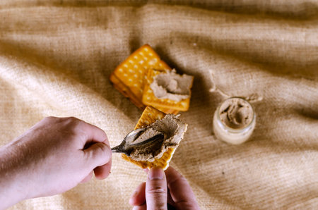 Close-up of a hand spreading pate on a cracker with a spoon. A man prepares himself an appetizer...