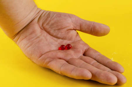 A hand and medical pills on a yellow background. Two red pills lie in the open palm of a man's hand. Health and medicine concept. Close-up. Selective focus.の写真素材