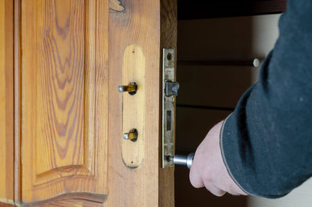 A man removes the old door lock. Hands with a screwdriver unscrew the mounting screws of the mortise...