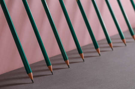 Geometric minimalistic composition with wooden pencils. Identical green pencils are leaning against a pink wall. Close-up. Selective focus.の写真素材