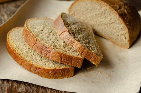 Close-up of three slices of bread on brown paper. Sliced loaf of rye bread on a wooden table....