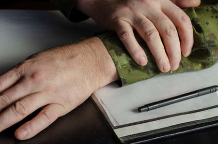 Officer's hands, document folder on black desk in close-up. A middle-aged man in a green camouflage uniform. Indoors. Selective Focus. Low key.の写真素材