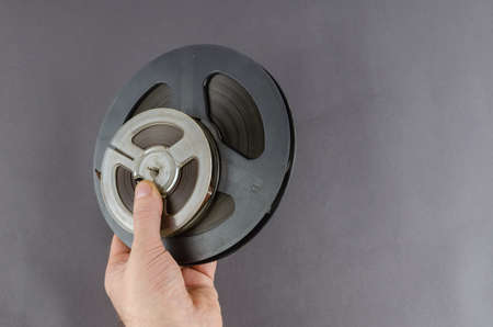 Old reels of music tape and hand on gray background. Man holding two Scuffed, scratched and dusty magnetic carriers of music recordings of the last century. Collecting concept.の写真素材